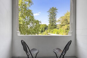 Une pièce avec une fenêtre donnant sur des arbres, deux chaises et un mur blanc.