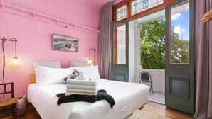 A bedroom with a large bed, a chair, a bedside table, and a window with a view of trees. - Heritage Apartment on City Fringe (Auckland)