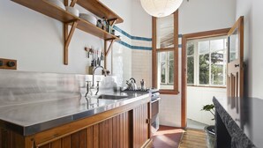 A kitchen with wooden cabinets, a stainless steel countertop, and a window providing natural light. - Heritage Apartment on City Fringe (Auckland)