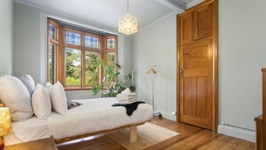 A bedroom with a bed, wooden floor, a hanging light fixture, a large window, and a wardrobe. - Heritage Apartment on City Fringe (Auckland)