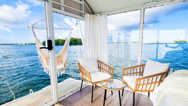 Ett rum med utsikt över havet, en hängmatta, två fåtöljer i rotting, ett litet runt bord och en säng.