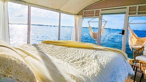 Ett sovrum med en stor säng, en hängstol och utsikt över havet.