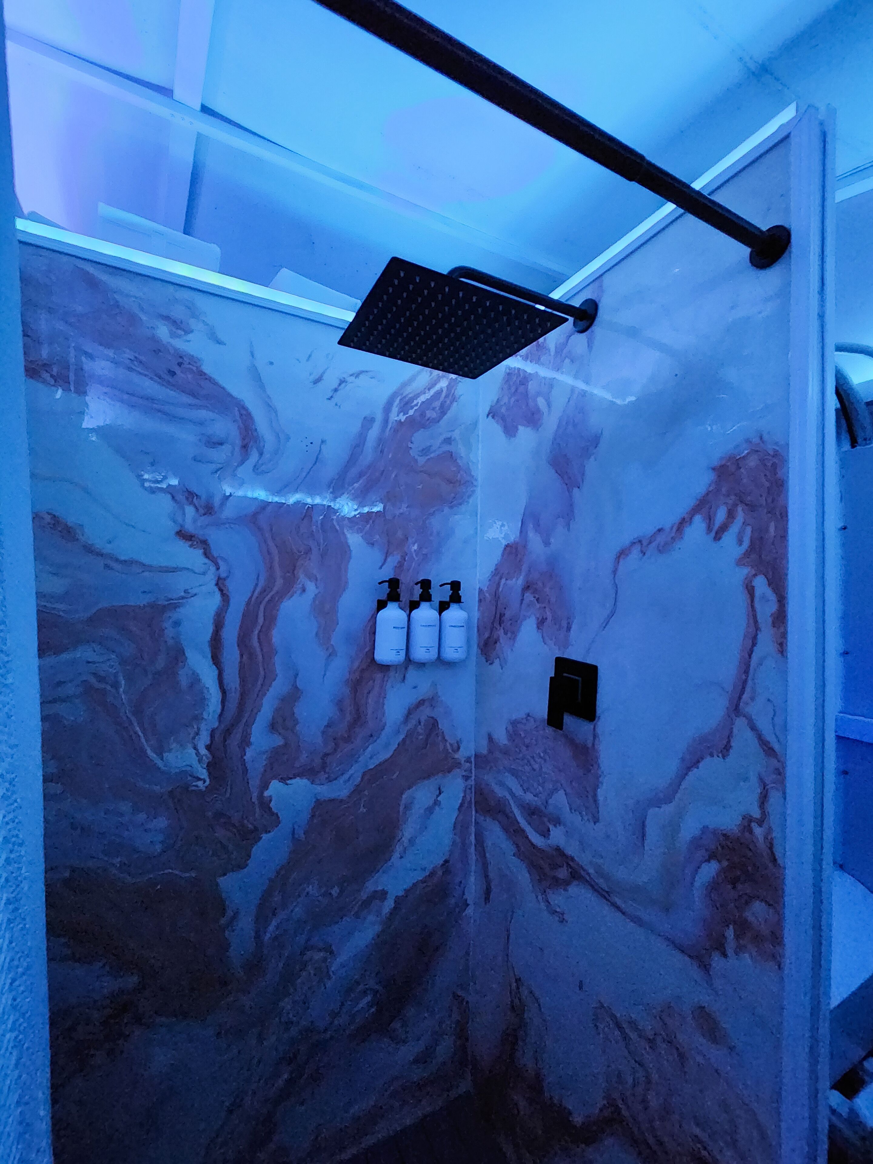 Une salle de bain avec un mur en marbre, une pomme de douche et trois bouteilles de shampoing.
