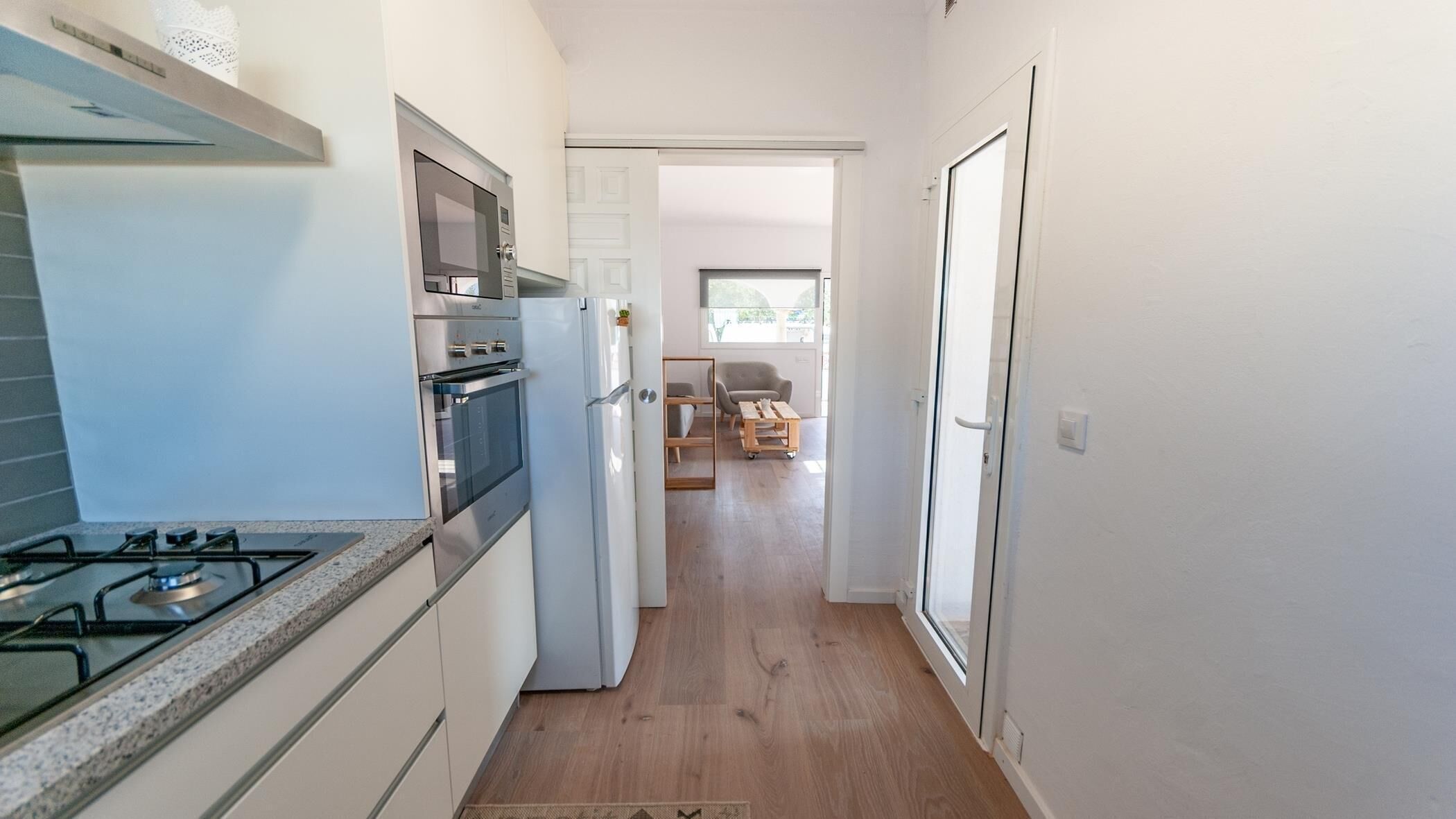 Une cuisine étroite équipée d’une cuisinière à gaz, d’un four et d’un réfrigérateur. On peut apercevoir une table et des chaises en bois dans la salle à manger adjacente.