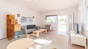 A modern living room with a sofa, two chairs, a coffee table, and a TV on a stand. - Vacay L’Escala - Casa Los Pinos, pool and tranquility (l'Escala)