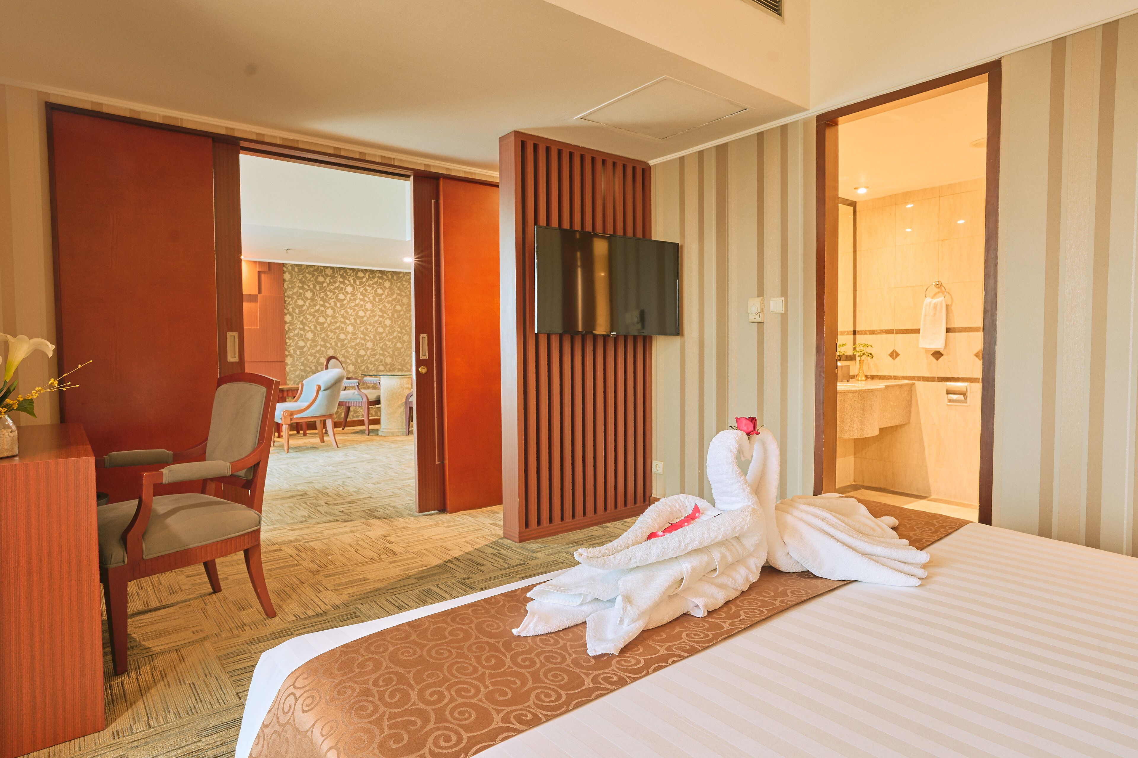 A hotel room with a bed, a desk, a chair, a TV, and a bathroom visible through an open door.