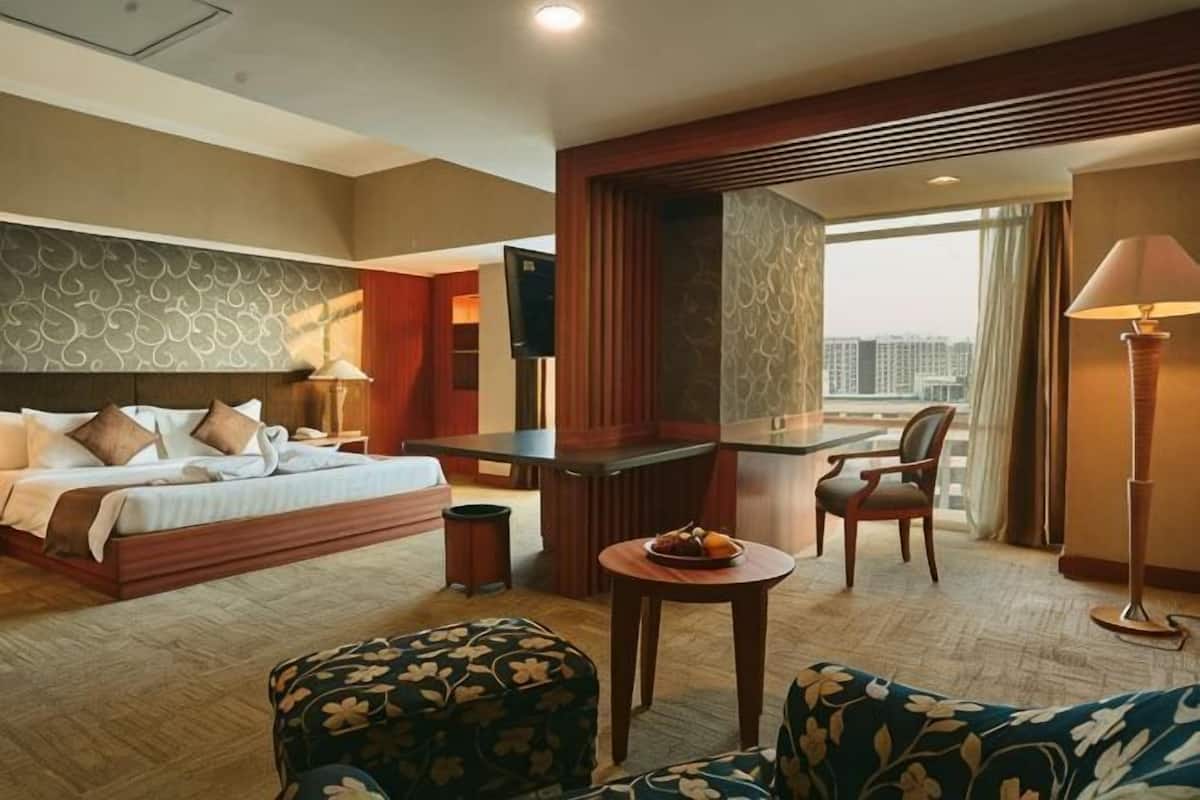 A hotel room with a bed, a desk, a chair, a sofa, and a view of the city.