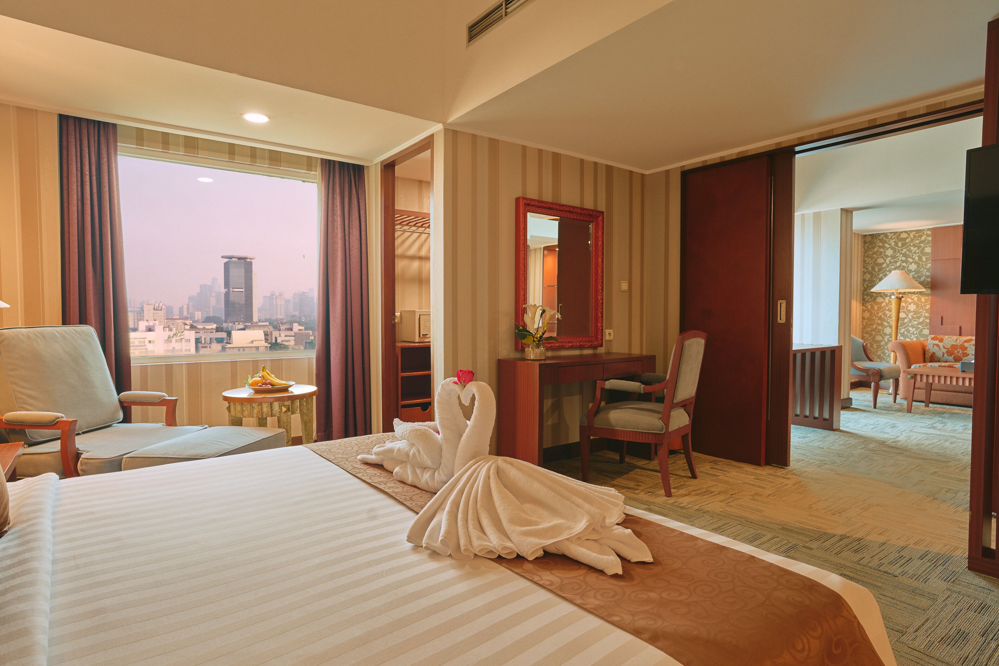 A hotel room with a large bed, a desk, a chair, and a view of the cityscape.