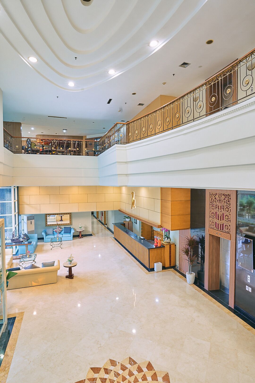 A spacious lobby with a reception desk, seating area, and a second-floor balcony with decorative railings.