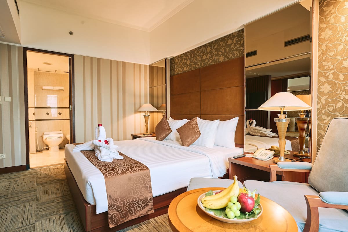 A hotel room with a large bed, two bedside tables, a desk with a chair, and a bathroom visible through an open door.