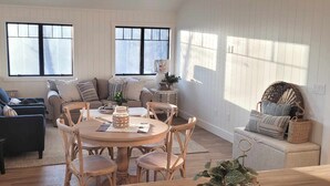 Un salon chaleureux avec une table ronde en bois, deux canapés et une table basse. Deux fenêtres laissent entrer la lumière naturelle.