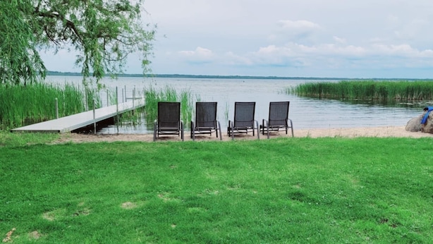 Une zone herbeuse avec une jetée menant à un plan d’eau, quatre chaises et une clôture blanche.