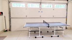 Une table de ping-pong dans un garage avec une porte et des fenêtres blanches.