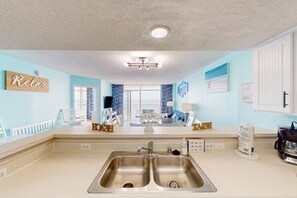 A modern kitchen with a double sink, a large window, and a view of the living area.
