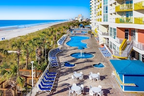 A resort pool area with a view of the beach, lounge chairs, and outdoor tables.
