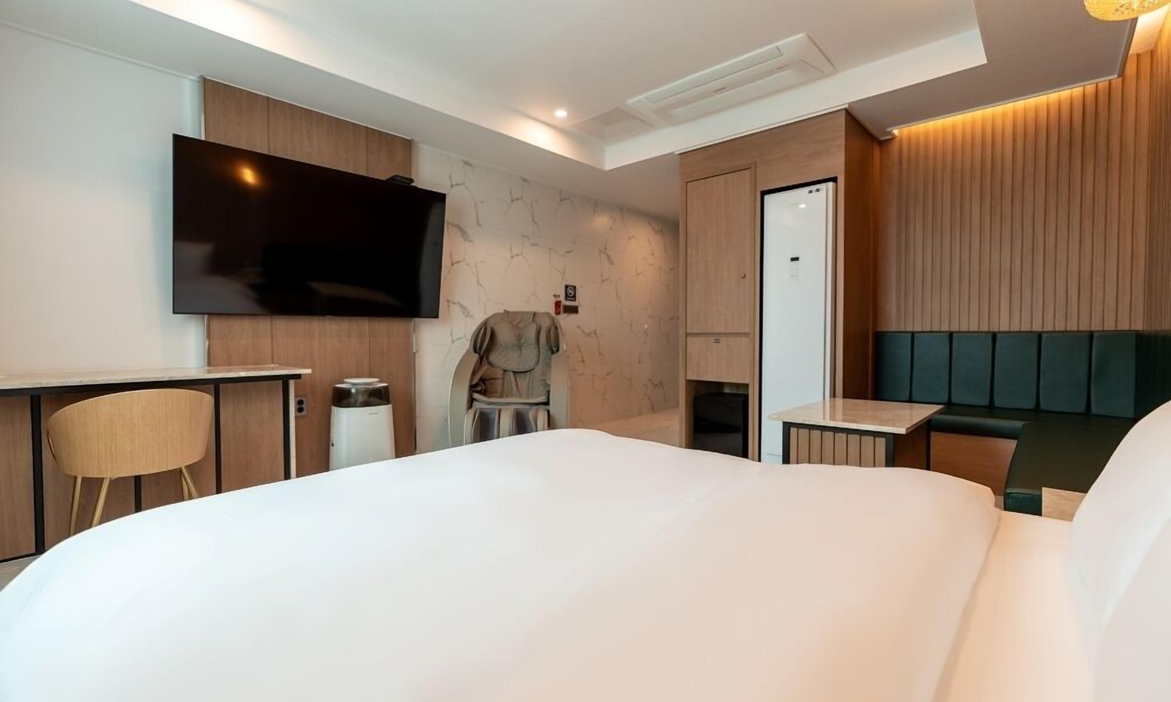 Una habitación de hotel moderna con una cama grande, un televisor de pantalla plana montado en la pared, una silla de masajes y una mesita pequeña.