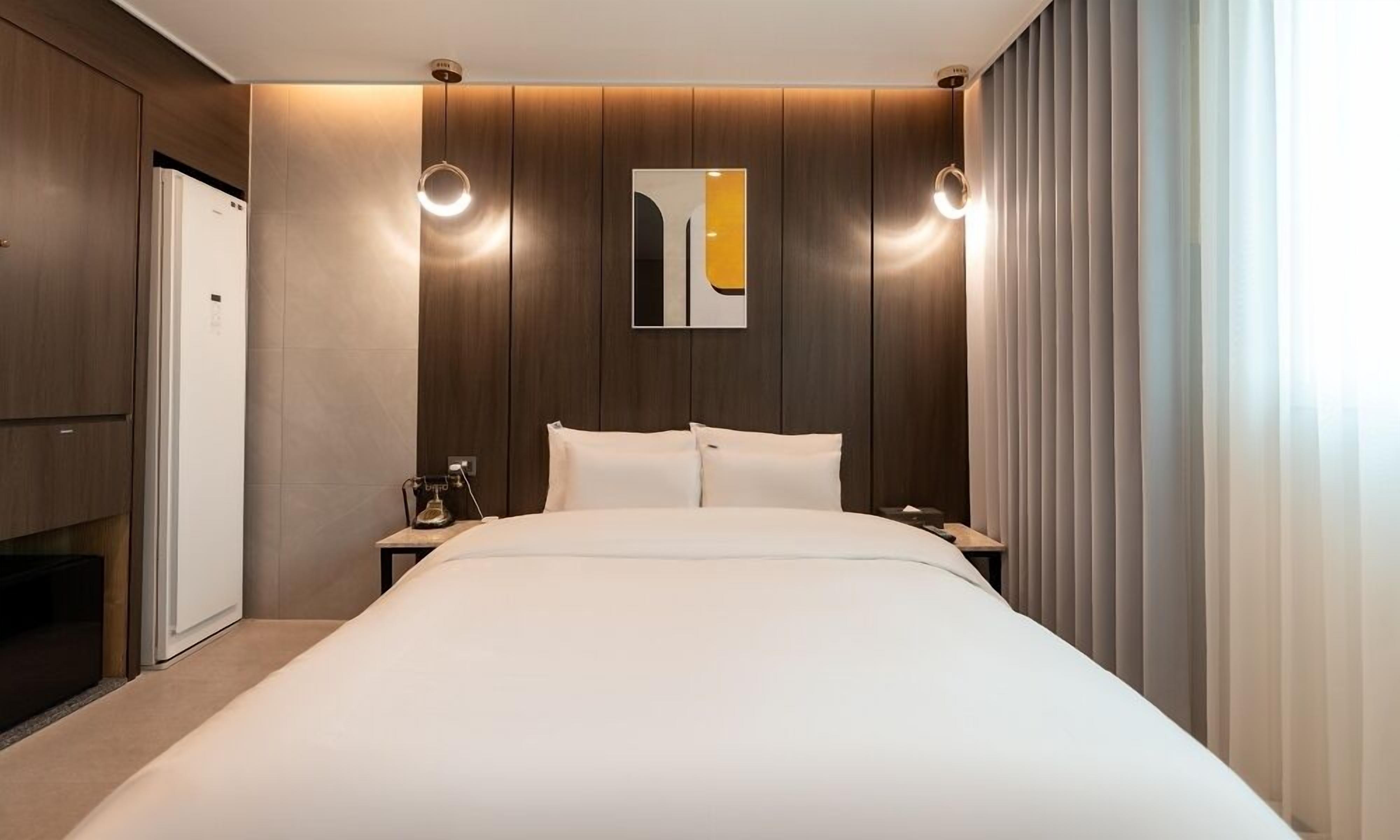 Una habitación de hotel moderna con una cama grande, una mesita de noche, una obra de arte en la pared y un ventanal con cortinas.