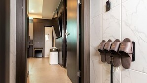 A hallway with a shoe rack holding multiple pairs of shoes, a trash bin, and a door leading to a room with a mirror and a light switch. - Jecheon Hound Hotel (Jecheon)