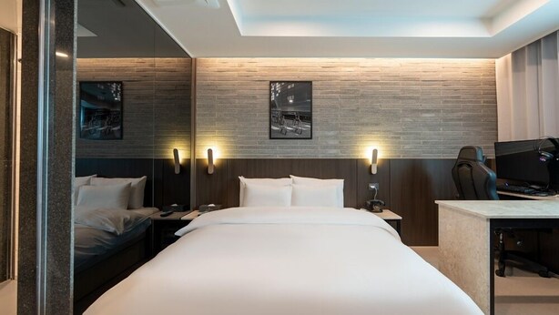 A modern hotel room with a large bed, a desk with a computer, and two wall-mounted lights. - Jecheon Hound Hotel (Jecheon)