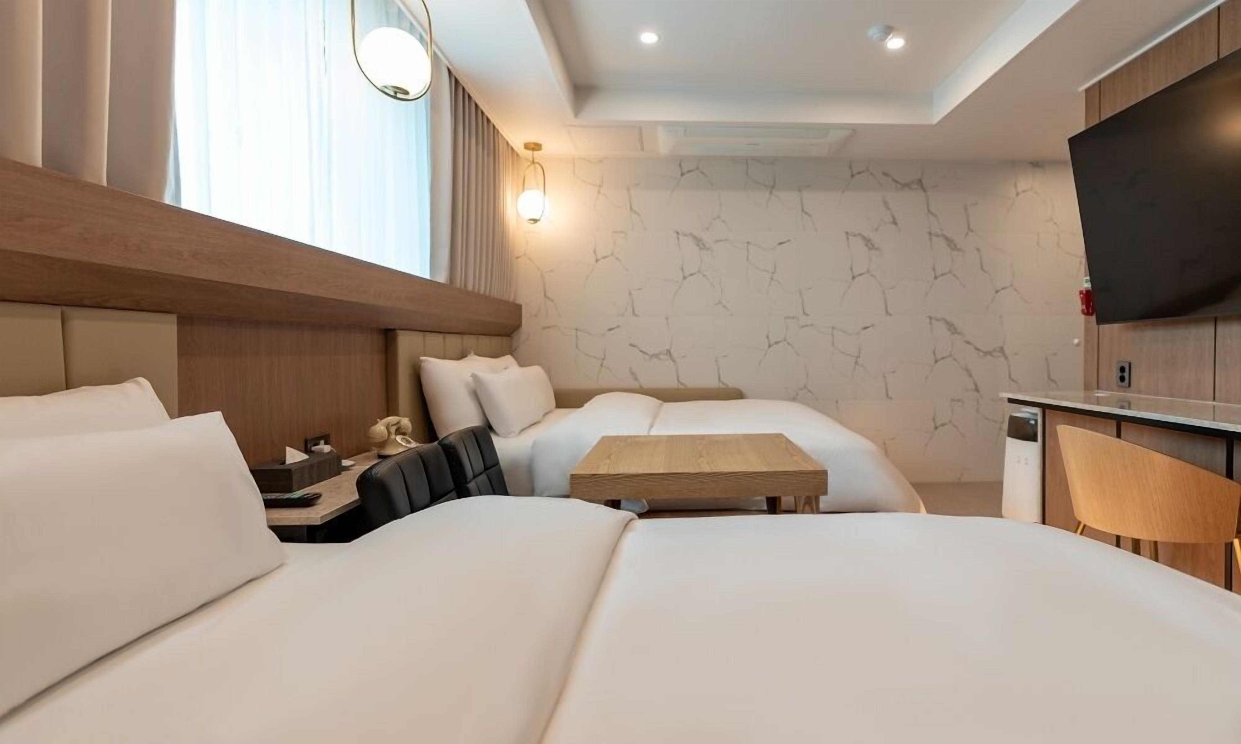 Una habitación de hotel moderna con una cama grande, una cama más pequeña, un escritorio y un televisor.