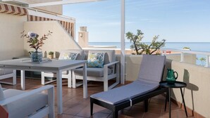 Eine Terrasse mit Tisch, Stühlen und einer Liege mit Blick auf das Meer.