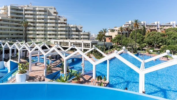 Ein Resort mit mehreren Schwimmbecken, weißen Poolgebäuden und hoch aufragenden Gebäuden im Hintergrund.