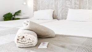 Uma cama bem arrumada com lençóis brancos, uma toalha bege e um pequeno cartão sobre a cama.