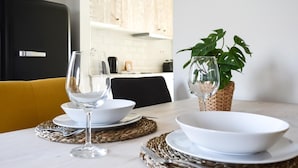 Mesa de jantar posta com pratos, tigelas e copos de vinho brancos, acompanhada por jogos americanos trançados.