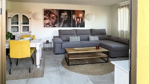 Uma sala de estar moderna com um sofá seccional cinza, uma mesa de centro de madeira e uma área de jantar com cadeiras amarelas.