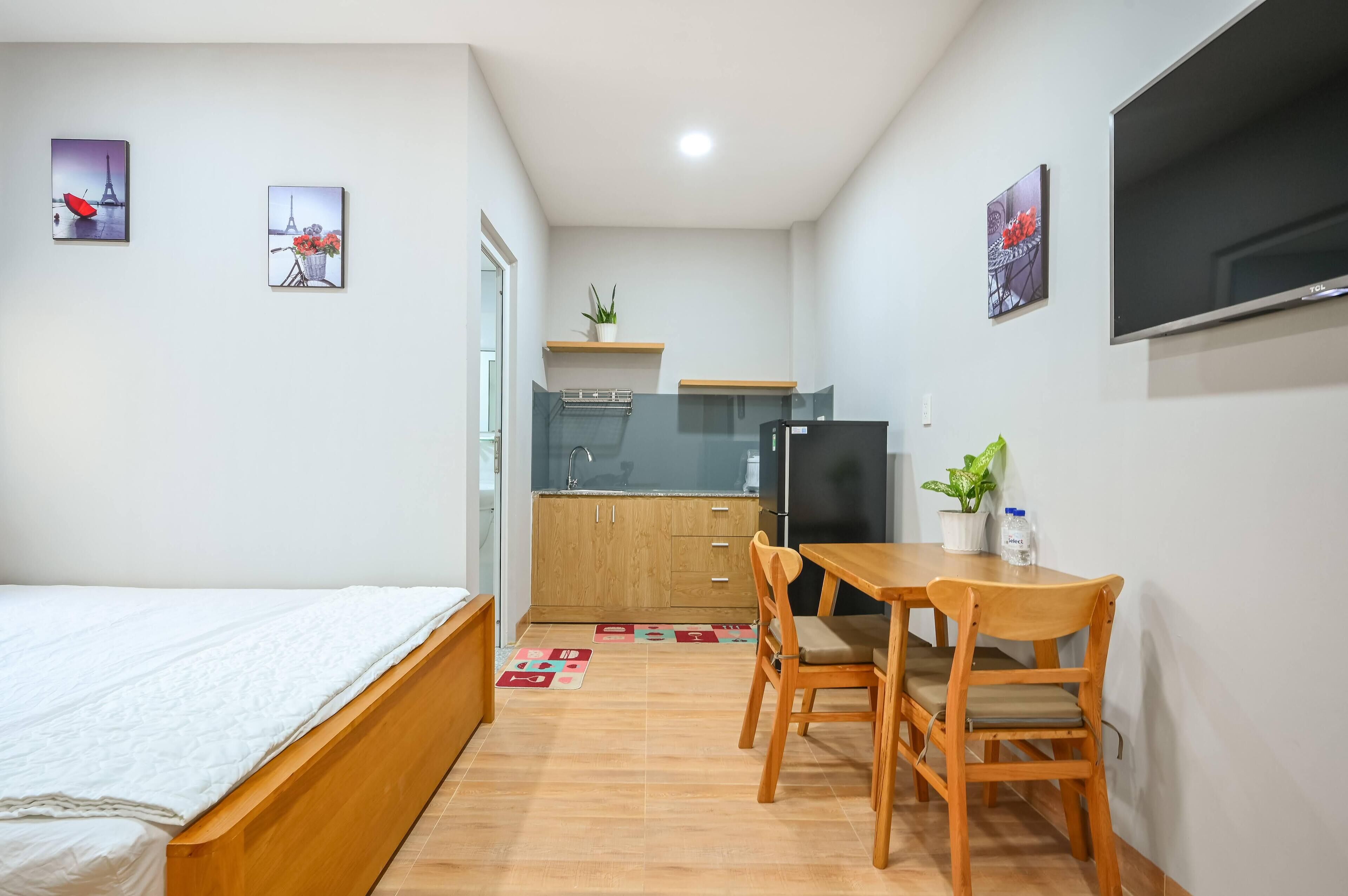A compact room with a bed, a small dining table with chairs, a TV, and a kitchenette.