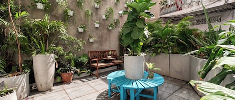 A courtyard with potted plants, a wooden bench, and a blue table.