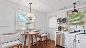 A kitchen with white cabinetry, a wooden dining table with chairs, a microwave, and a sink. - Stylish 1BR Apartment in Cape May (Cape May)