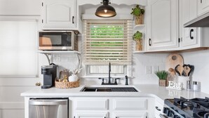 A modern kitchen with white cabinetry, a built-in microwave, a stainless steel dishwasher, a gas stove, and a window with blinds. - Stylish 1BR Apartment in Cape May (Cape May)