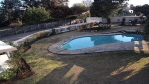 A backyard with a swimming pool, surrounded by a fence and various trees. - 5 Bed House - Sleeps 10 - Pool - Parking - Wifi (Nigel)