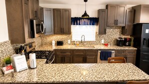 A kitchen with granite countertops, dark wood cabinets, stainless steel appliances, and a central island with bar stools. - Quiet Farm Guesthouse Near Lake Houston (Crosby)