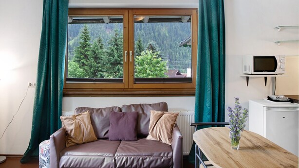 A room with a wooden-framed window, a brown leather sofa, a small table, and a white microwave.