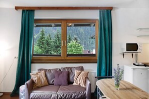 Una habitación con ventana de madera, un sofá de cuero marrón, una mesita y un microondas blanco.