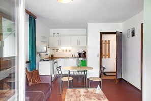 A compact living space with a kitchenette, a dining area with a table and chairs, a sofa, and a glass partition.