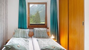 A bedroom with two beds, a window with a mountain view, and a wooden wardrobe.