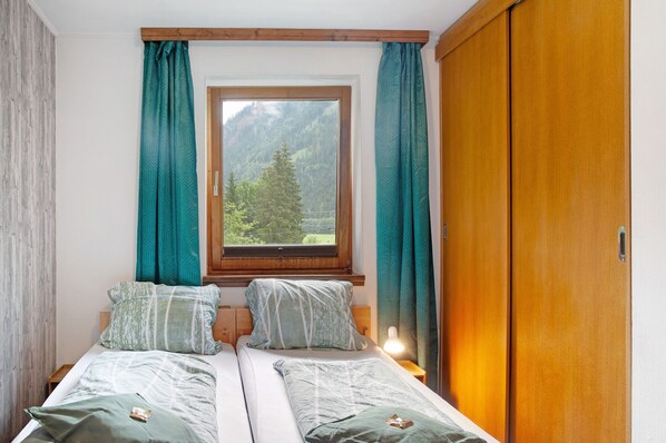 A bedroom with two beds, a window with a mountain view, and a wooden wardrobe.