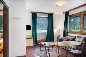 A room with a wooden table, a sofa, a TV, and a window with curtains.