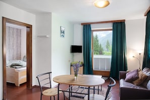 A room with a bed, a round table with chairs, a TV, and a window with curtains.