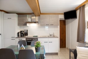 A compact kitchen with a dining table, chairs, a coffee maker, and a television mounted on the wall.