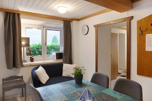 A room with a bed, a dining table, a clock, and a window with curtains.