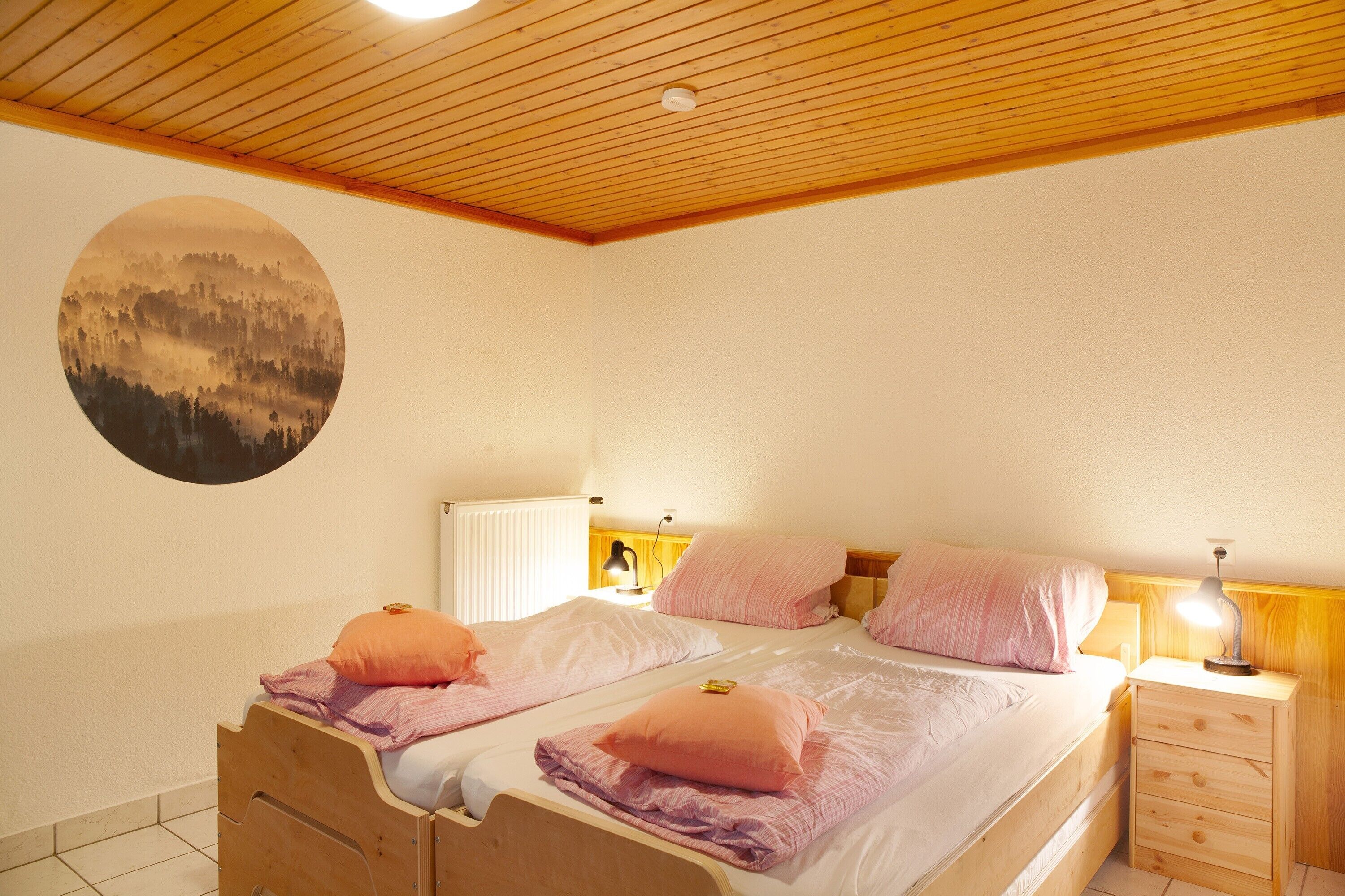 Une chambre avec deux lits, des têtes de lit en bois, des tables de chevet avec des lampes et une œuvre d’art circulaire fixée au mur.