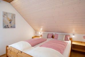 Une chambre avec un plafond en bois, deux lits avec une literie à carreaux, une table de chevet et une lampe fixée au mur.