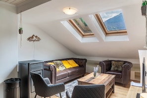 A loft-style room with a brown leather sofa, two armchairs, a wooden coffee table, and skylights.
