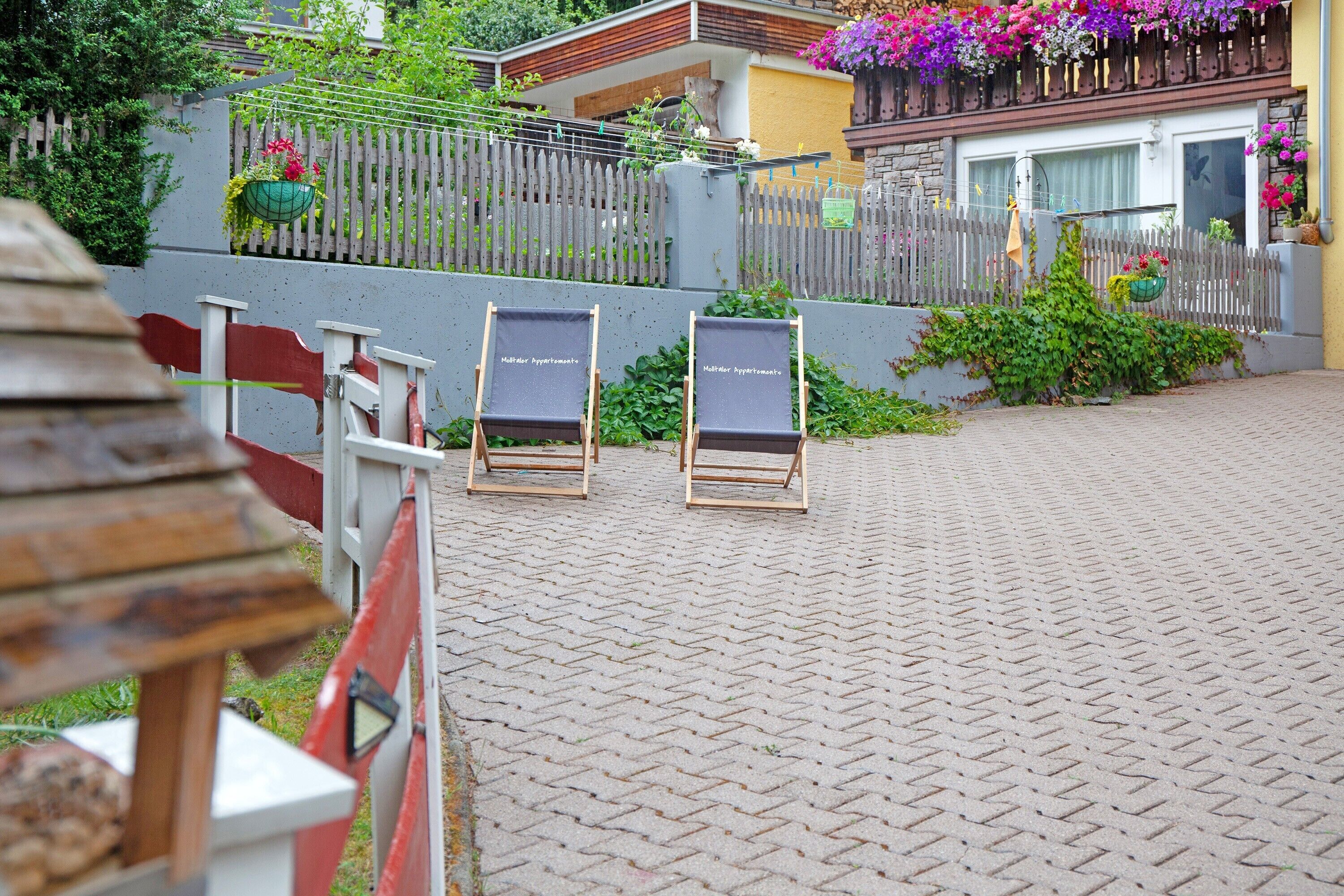 A paved pathway leading to a building with a wooden fence and hanging flower baskets.