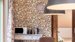 Una habitación con una pared de troncos apilados, un reloj, un microondas, una tetera, una mesa de madera y una silla marrón.