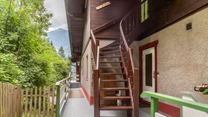 Una escalera de madera que conduce a un edificio con una puerta roja y barandilla de madera.